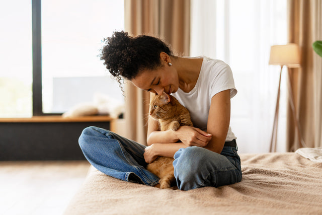 Cat parent cuddling an orange tabby cat at home